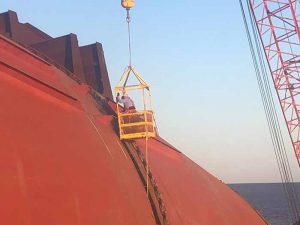 Technicians on side of ship in basket