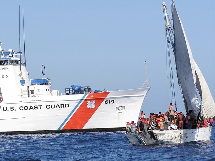 maritime border enforcement scene showing USCG cutter stopping overloaded boat