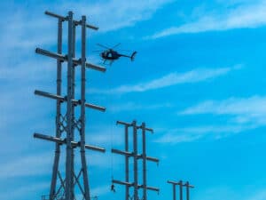 A lineman, lifted by helicopter, installs hardware to support raising the transmission lines to provide 205 feet of operational clearance for larger vessels calling JAXPORT’s Blount Island terminal. [Photo: JAXPORT]
